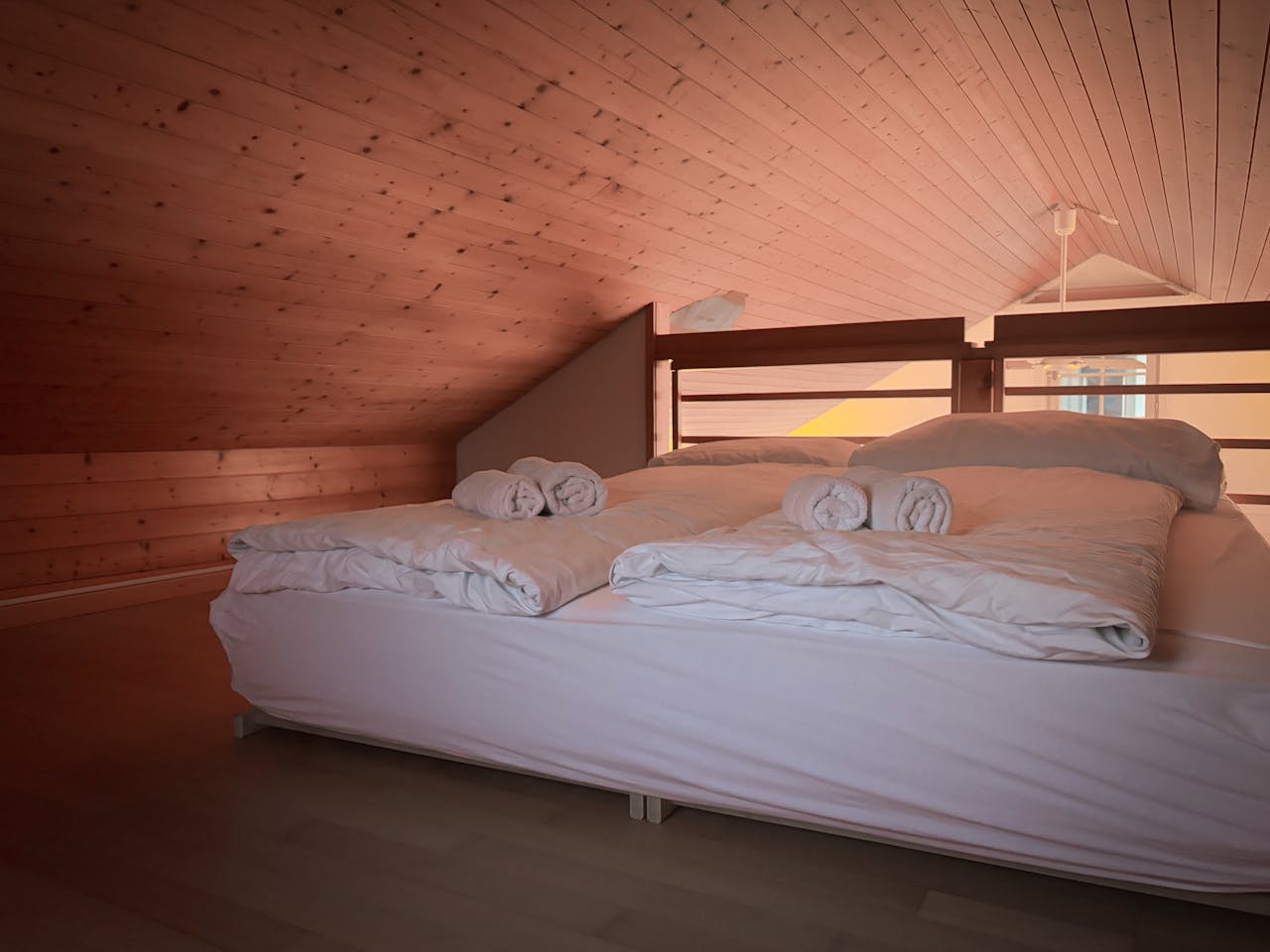 services-01 Warm, inviting loft bedroom featuring wooden ceiling and fresh linens.