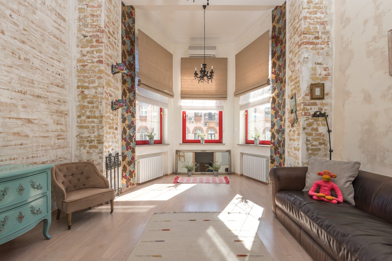 Interior of cozy room with comfortable couches and chest of drawers placed at ornamental walls with sun shining through window with jalousie